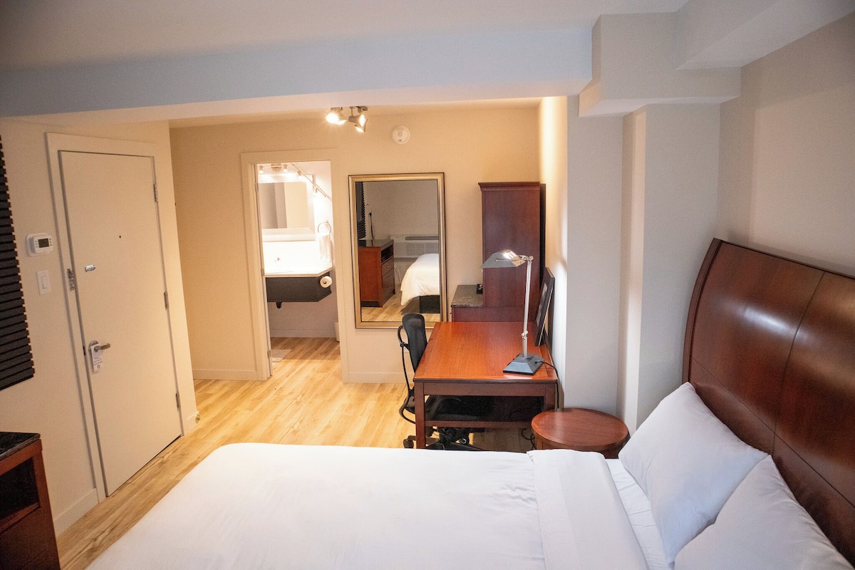 A hotel room with a bed, desk, chair, and a mirror.