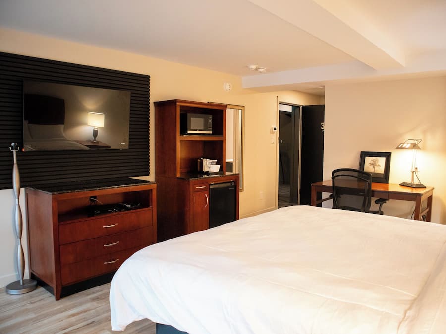 Een hotelkamer met een bed, een bureau, een stoel, een televisie, een magnetron en een kledingkast.