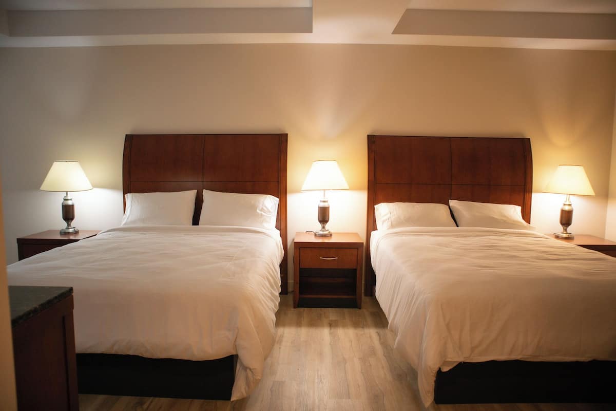 A hotel room with two beds, wooden headboards, bedside tables with lamps, and a wooden floor.
