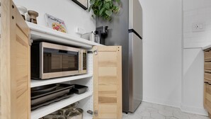 A kitchen with a microwave, oven, and stainless steel appliances. There is a wooden cabinet with a plant on top. - Sherbrooke 101 Downtown Montreal | Balcony, Queen Bed, Sofa Bed, Parking & TV (Montréal)