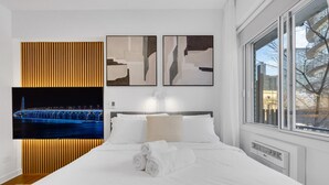 A modern hotel room with a large bed, a view of the city through the window, and abstract wall art. - Sherbrooke 101 Downtown Montreal | Balcony, Queen Bed, Sofa Bed, Parking & TV (Montréal)
