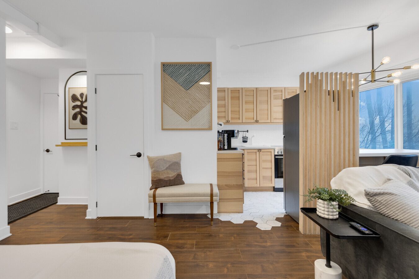 Un dormitorio moderno y funcional con cama, mesita de noche y vistas a una cocina y sala de estar.