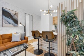 Ein modernes Wohnzimmer mit einer Couch, zwei Barhocker, einem Couchtisch und einer Pendelleuchte.