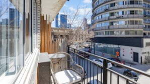 A balcony with a chair, a view of a multi-story building, and parked cars.