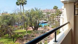A view of a hotel courtyard with a swimming pool, palm trees, and a building with balconies. - Apartment Castle Harbour (Arona)