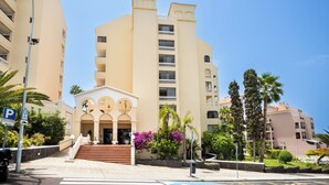 A multi-story hotel with a central entrance, balconies, and surrounding greenery. - Apartment Castle Harbour (Arona)