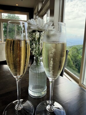 Deux flûtes à champagne sont posées sur une table, et par la fenêtre, on peut admirer le paysage extérieur.