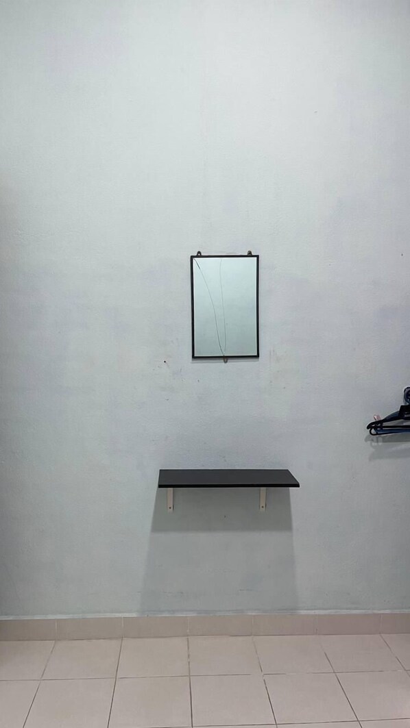 Una habitación con una pared sencilla, un estante negro pequeño y un espejo enmarcado.