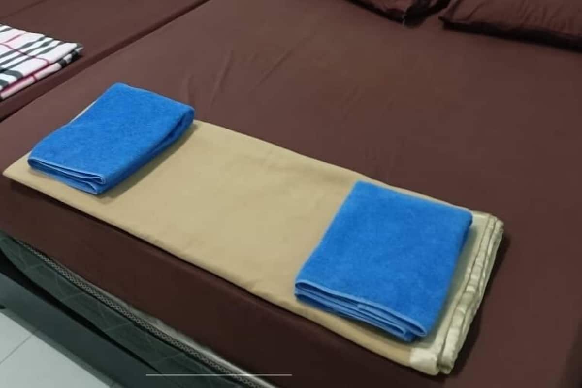 Una cama doble con ropa de cama marrón y dos toallas azules, un cuadro de una bicicleta en la pared y un enchufe en la pared.