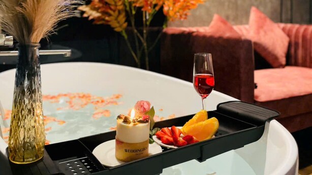 Una mesa con una vela, una botella de Widdington y fruta, frente a un sofá rosa y flores otoñales.