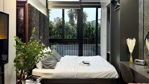 Un dormitorio moderno con cama, mesita de noche, televisor y ventana con vistas a zonas verdes.