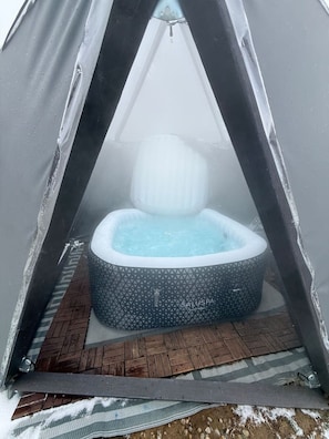 A hot tub inside a tent with a patterned exterior, a wooden floor, and a visible logo.