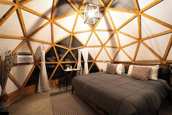 A room with a geometric wooden ceiling, a bed with pillows, a table with chairs, and a hanging light fixture.