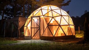 Une tente en forme de dôme géodésique, illuminée la nuit, offrant une vue dégagée sur les étoiles.