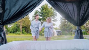 Deux personnes se dirigent vers un espace extérieur équipé d’un jacuzzi, avec un gazebo en arrière-plan.