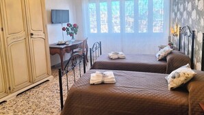 A hotel room with two beds, a desk, a chandelier, and a large window with a view. - A Casa di Noele (Roma)