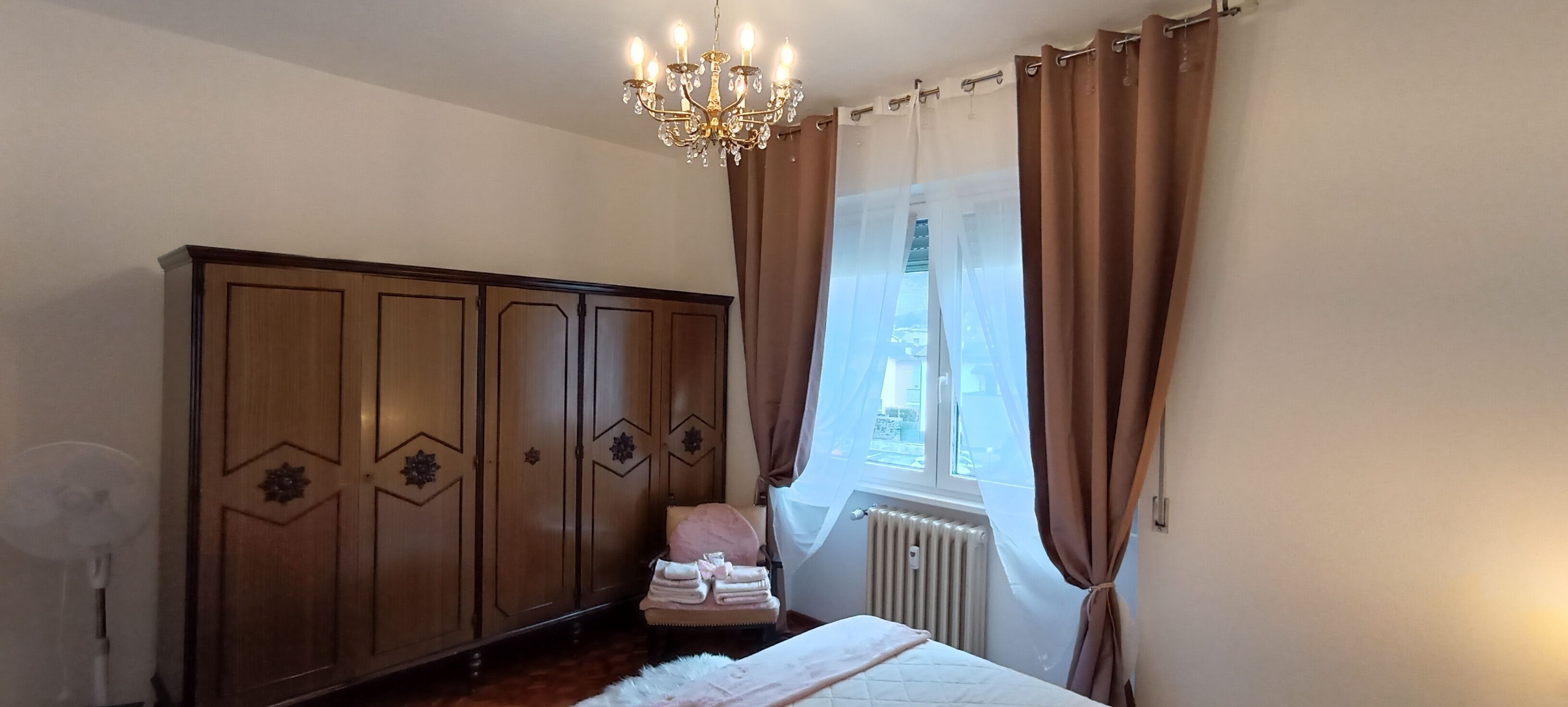 Een slaapkamer met een grote kledingkast, een fauteuil, een radiator en een raam met gordijnen.