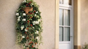 Un arrangement floral fixé au mur, une table blanche pour l’extérieur avec une bougie, et deux chaises blanches.