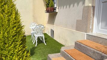 Un petit espace extérieur privé, agrémenté d’une pelouse verdoyante, d’un banc en métal blanc et d’une plante en pot.