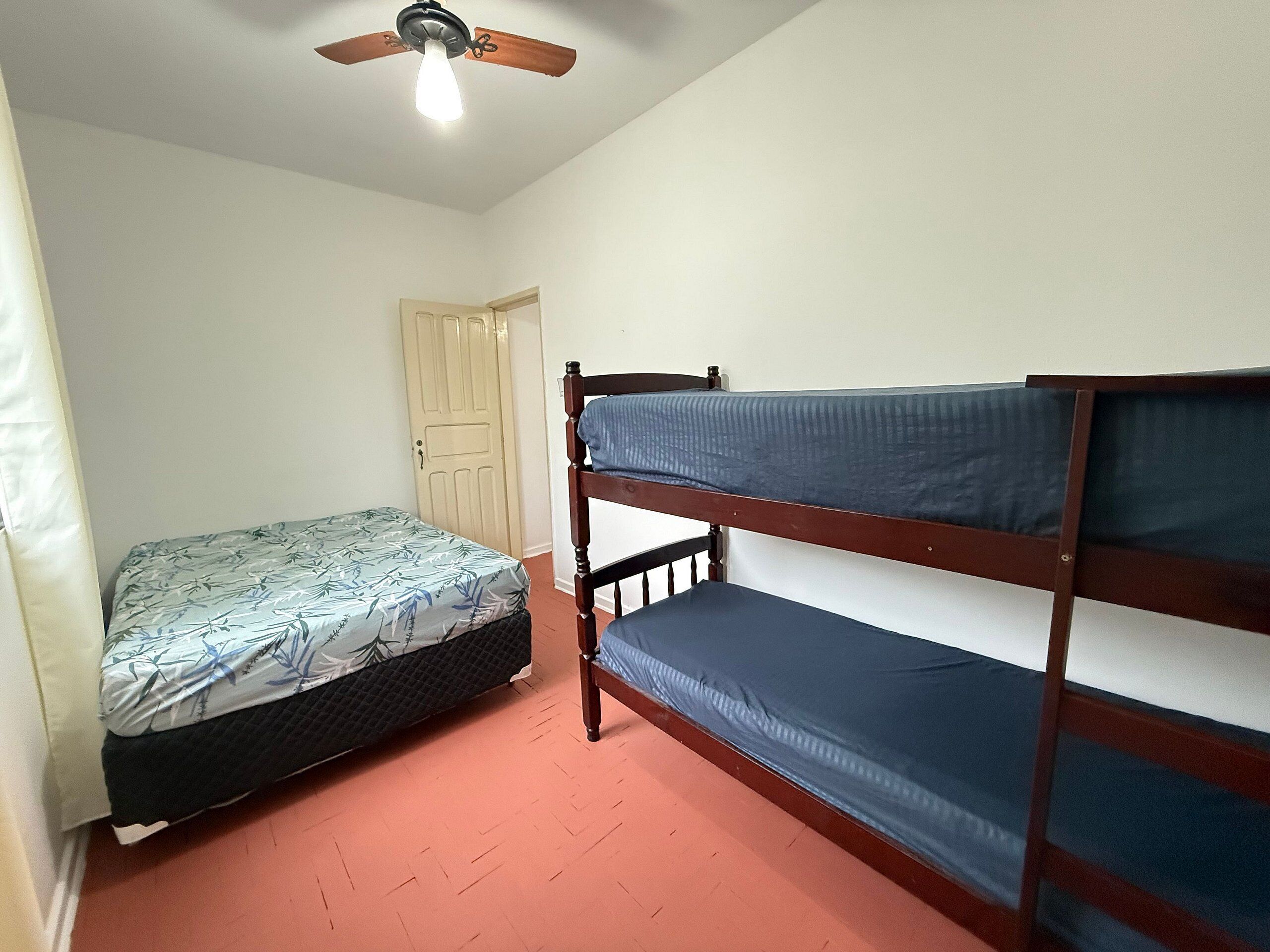 Una habitación pequeña con una cama individual, una litera, un ventilador de techo y una puerta.