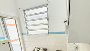 Una cocina compacta con estufa a gas, un lavamanos y un ventanal con persianas.