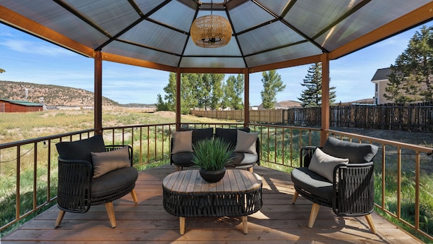 A covered outdoor seating area with two chairs and a table, surrounded by a wooden deck and a metal railing. - Bunny's Ranch (Big Bear City)