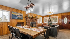 A wooden-paneled room with a fireplace, a dining table with chairs, a Christmas tree, and a large window. - Bunny's Ranch (Big Bear City)