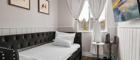 A bedroom with a bed, ceiling fan, artwork, and a window with curtains.