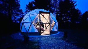 A geodesic dome structure with a door open, revealing an interior with a bed and a table.