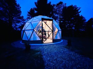 A geodesic dome structure with a door open, revealing an interior with a bed and a table.