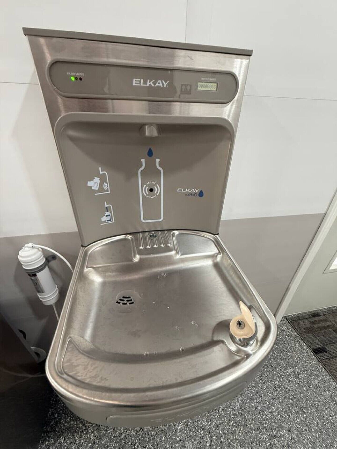 A modern, stainless steel toilet with a control panel and water bottle holder.
