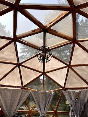 A geodesic dome structure with a central hanging light fixture and curtains at the bottom.