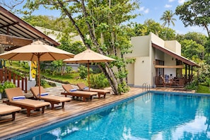 A poolside area with lounge chairs and umbrellas, surrounded by lush greenery and a modern building. - Nature Surf Villas (Dikwella)