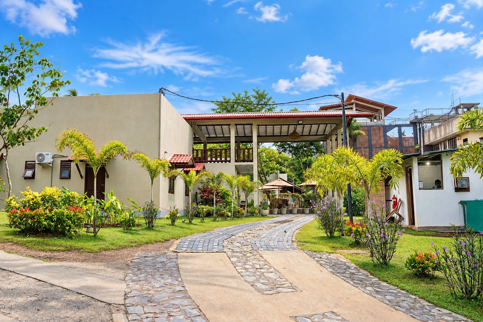 A building with a covered walkway, surrounded by greenery and a paved path.