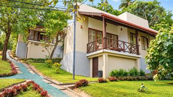 A two-story building with a balcony, surrounded by a well-maintained garden with a paved walkway.