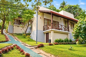 A two-story building with a balcony, surrounded by a well-maintained garden with a paved walkway. - Nature Surf Villas (Dikwella)