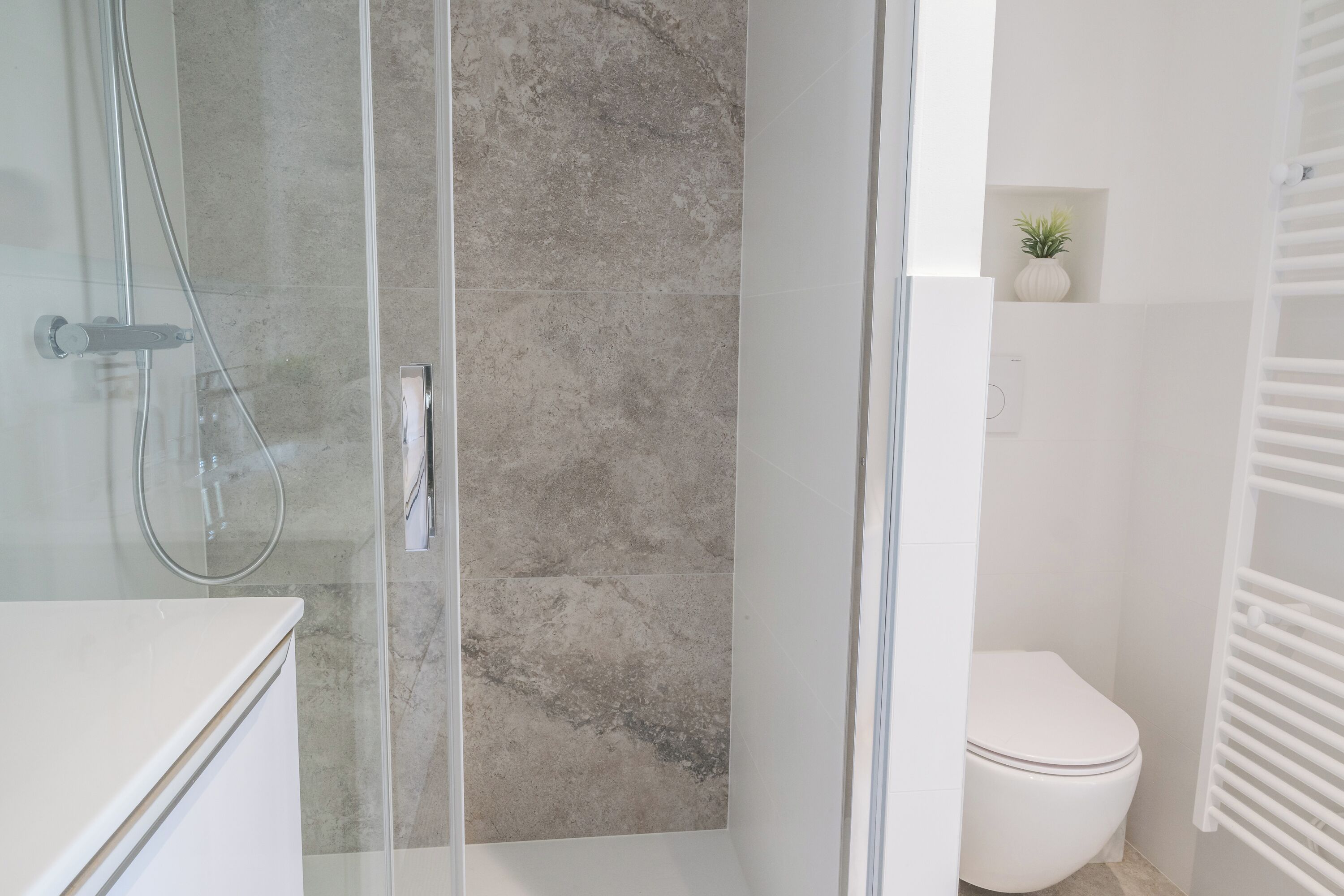 Un baño moderno con cabina de ducha de vidrio, inodoro blanco y una pequeña planta en maceta en la pared.