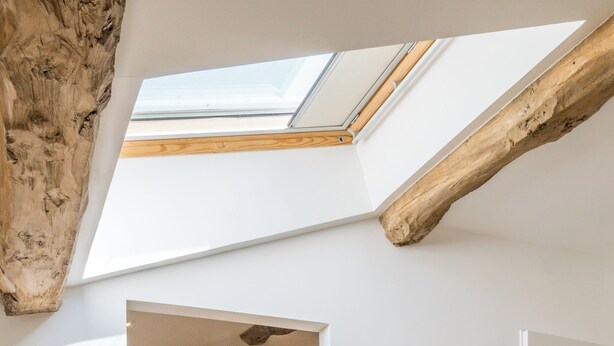 A room with a skylight, wooden beams, a white door, a white wall, a wooden floor, and a basket. - Les Tamaris (SAINTE TERRE)