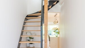 A modern staircase with wooden steps and a metal handrail, leading to a bright room with a window and a hanging light fixture. - Les Tamaris (SAINTE TERRE)