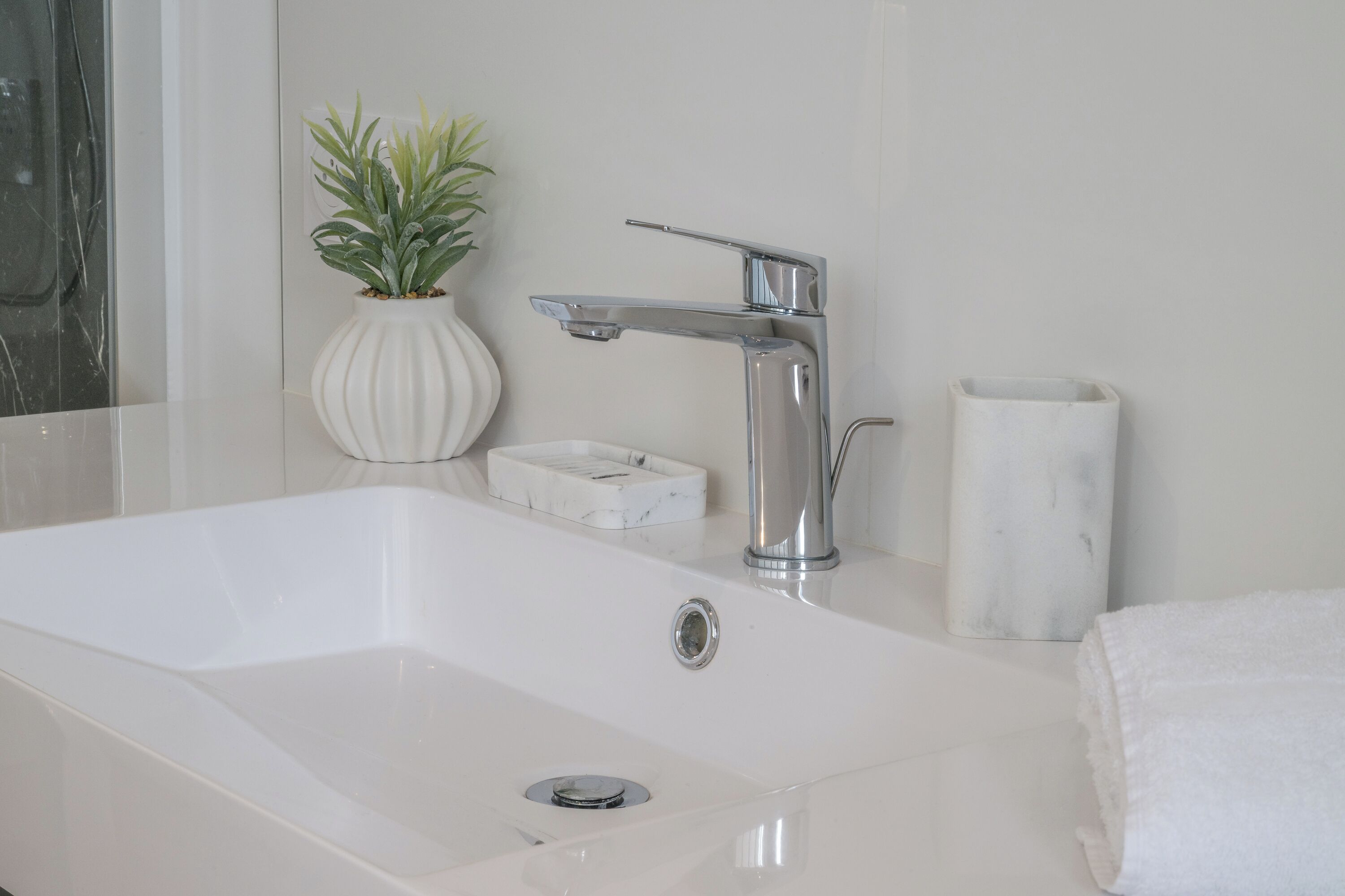 A modern bathroom with a white sink, chrome faucet, and a potted plant.