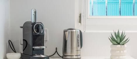 Una encimera de cocina con una cafetera, un hervidor, un bol y una planta en maceta.