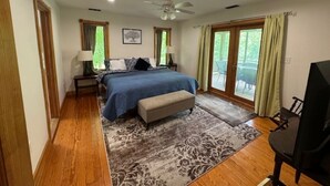 A bedroom with a bed, bedside tables, a desk, a chair, a ceiling fan, and large windows. - Tranquil Cardinal Hill Cabin- Perfect for Relaxation & Exploration. Pet Friendly (Sperryville)