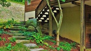 A garden with a stone staircase leading to a wooden door, surrounded by greenery and rocks. - Tranquil Cardinal Hill Cabin- Perfect for Relaxation & Exploration. Pet Friendly (Sperryville)