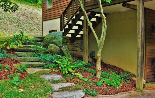 Ein Garten mit einer Steintreppe, die zu einer Holztür führt, umgeben von viel Grün und Steinen.