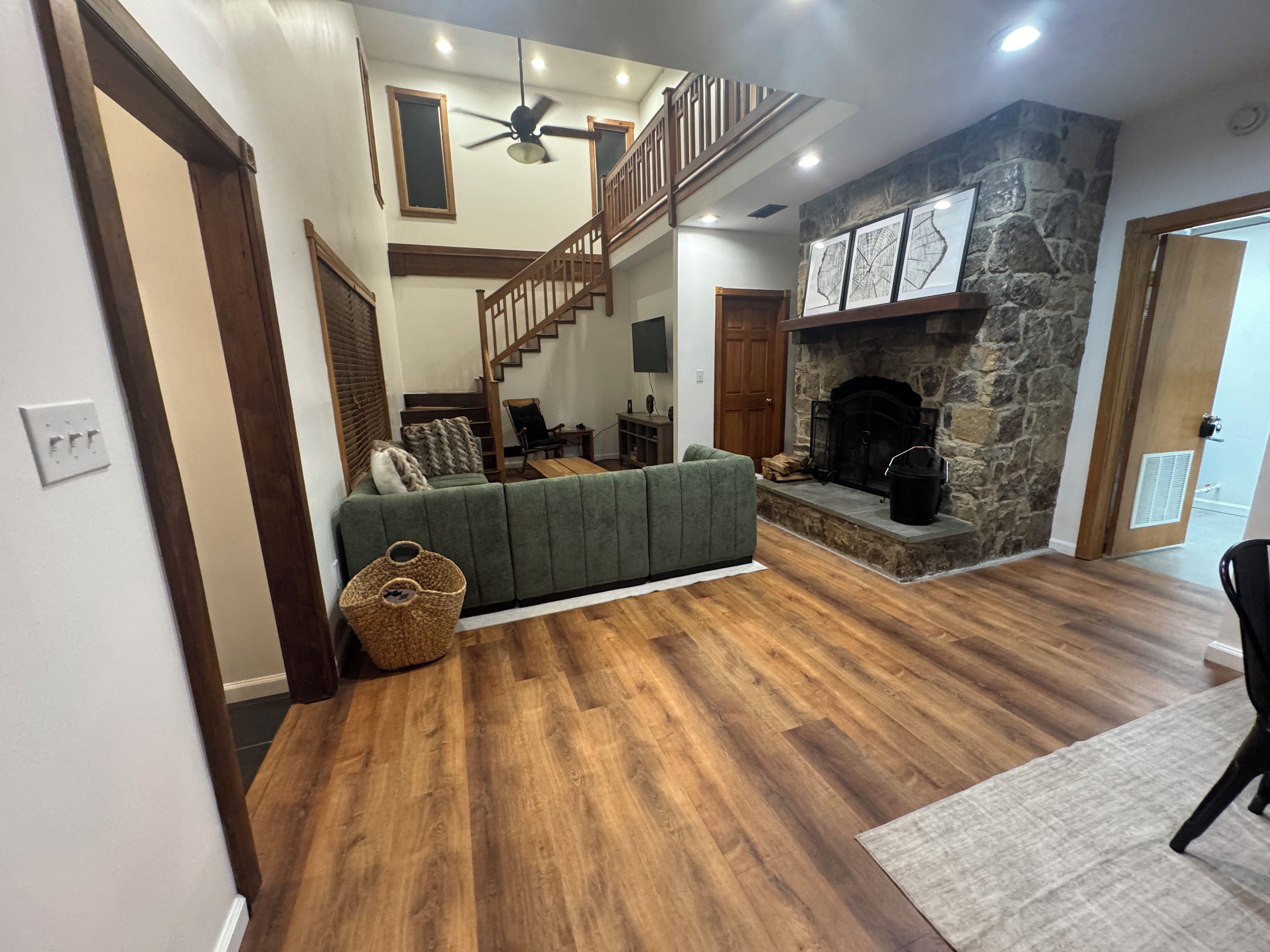 A spacious living area with a green sofa, wooden flooring, a stone fireplace, and a staircase.