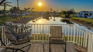 A wooden deck with a hammock chair and a lounge chair overlooking a calm pond and a residential area during sunset. - Pond View 2BR 2BA Beach Escape (Fort Myers Beach)