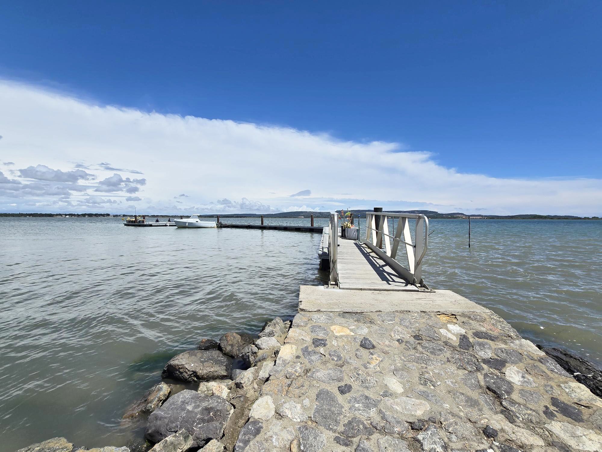 A stone pier extending into calm water with a clear sky above.