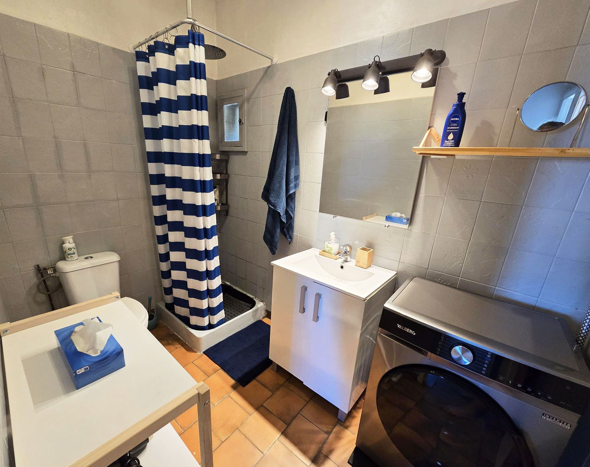 A compact bathroom with a shower, toilet, sink, and washing machine.