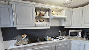 Uma cozinha com armários brancos, fogão a gás, micro-ondas e luminária pendente.
