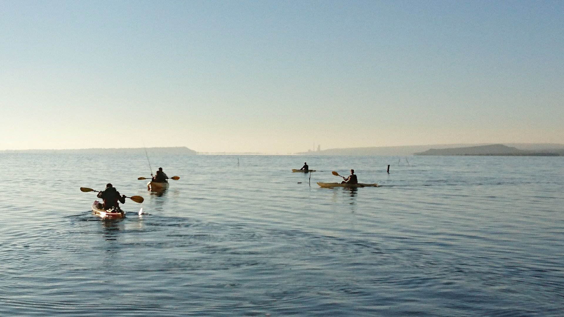 A calm sea with kayaks and a distant shoreline.